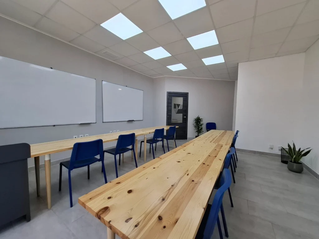 Aula de JG Academia con mesas de madera, sillas azules y dos pizarras blancas